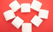 Top view of white toilet paper rolls arranged in heart on red background