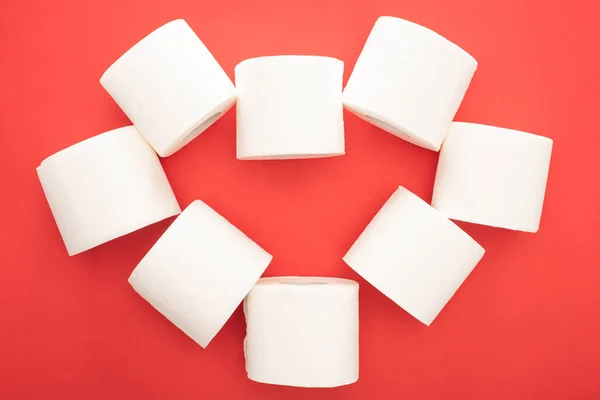 Top view of white toilet paper rolls arranged in heart on red background