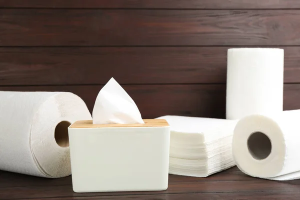 Clean napkins, box with tissues and rolls of paper towels on wooden table